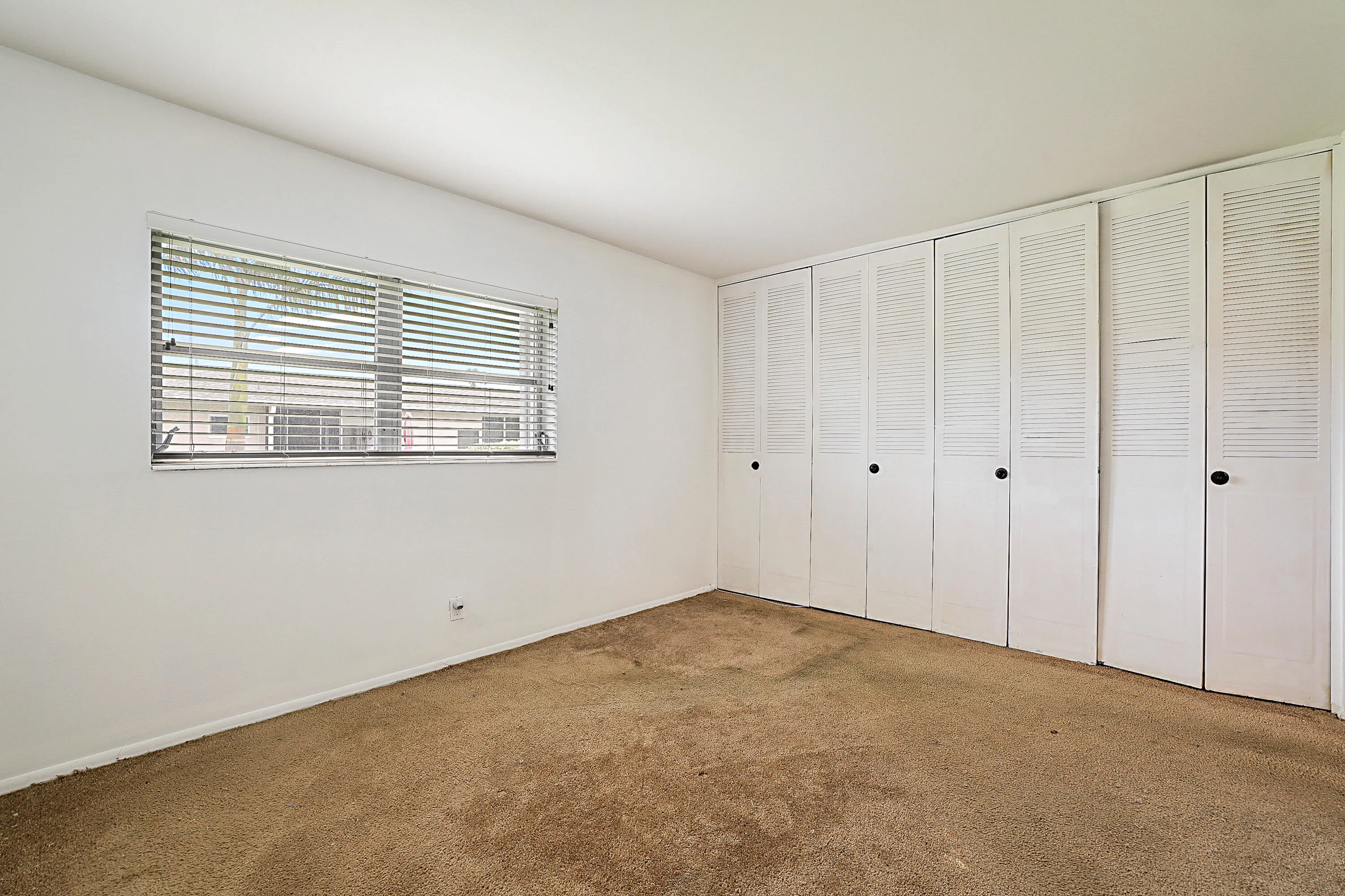 White walls, horizontal window blinds, and built-in louvered closet doors