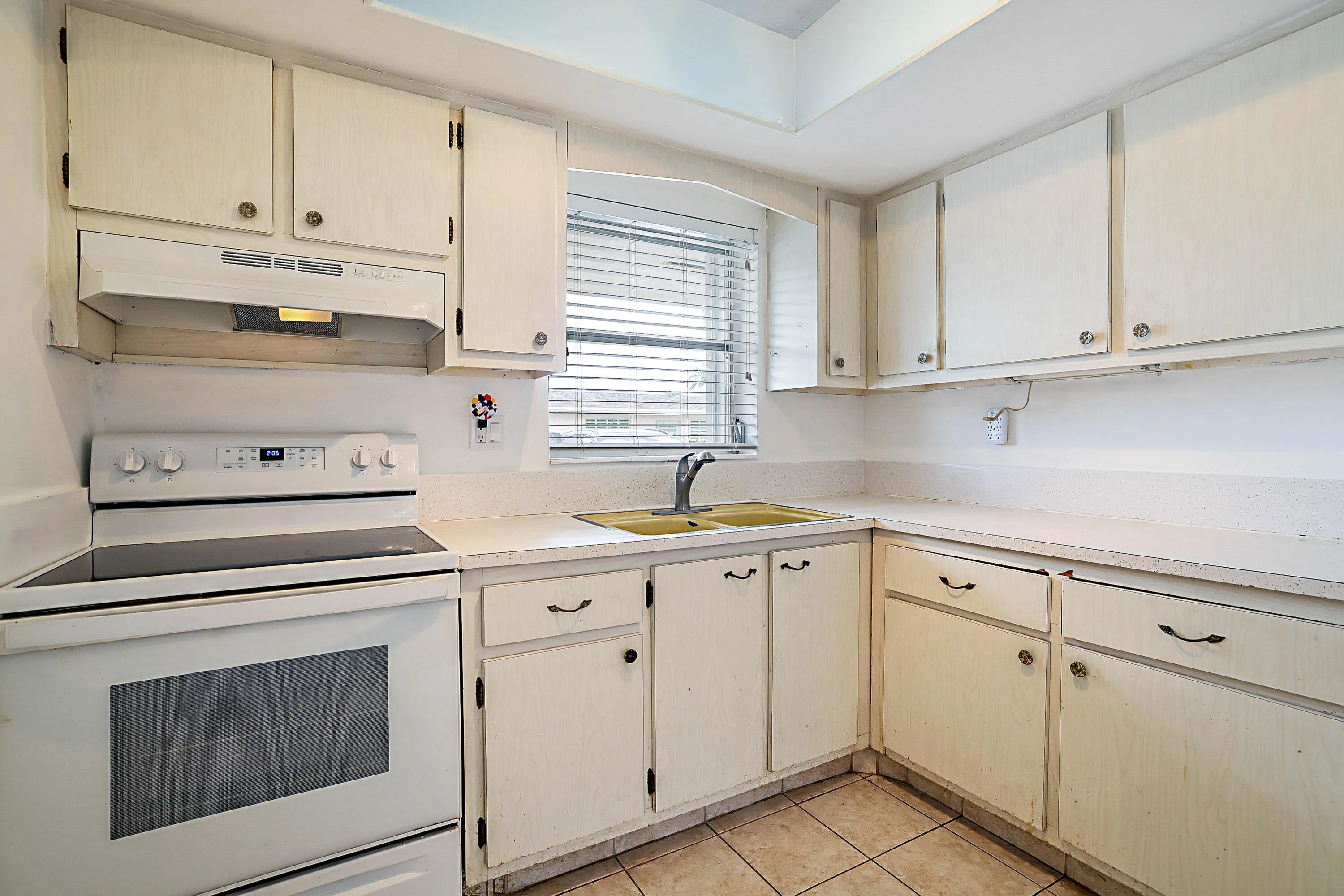 Kitchen with white cabinetry, a built-in range, a double basin sink, and tiled flooring