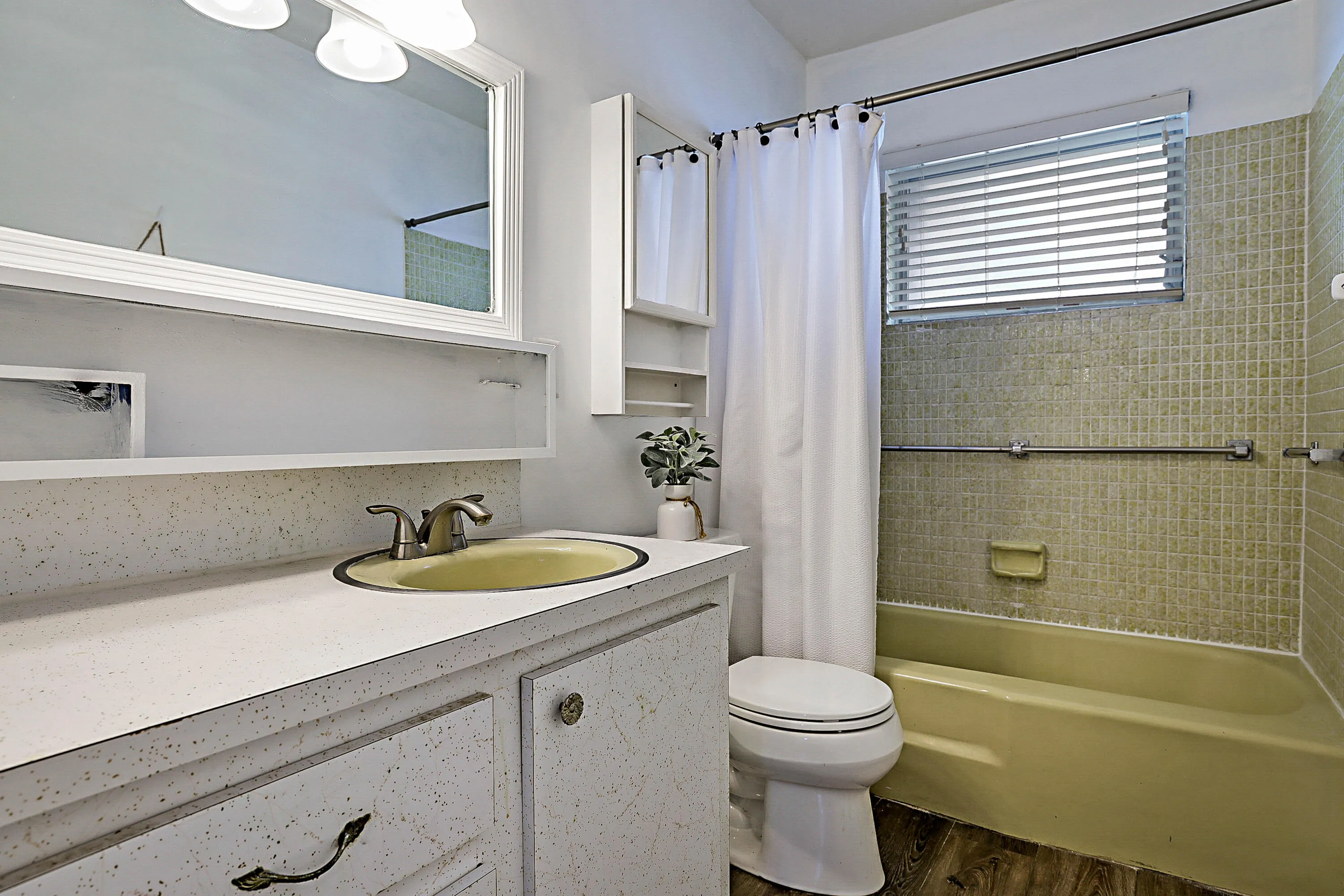 Bathroom featuring a bathtub with tiled surround, a vanity with an integrated sink, a wall-mounted mirror, and wood-finish flooring