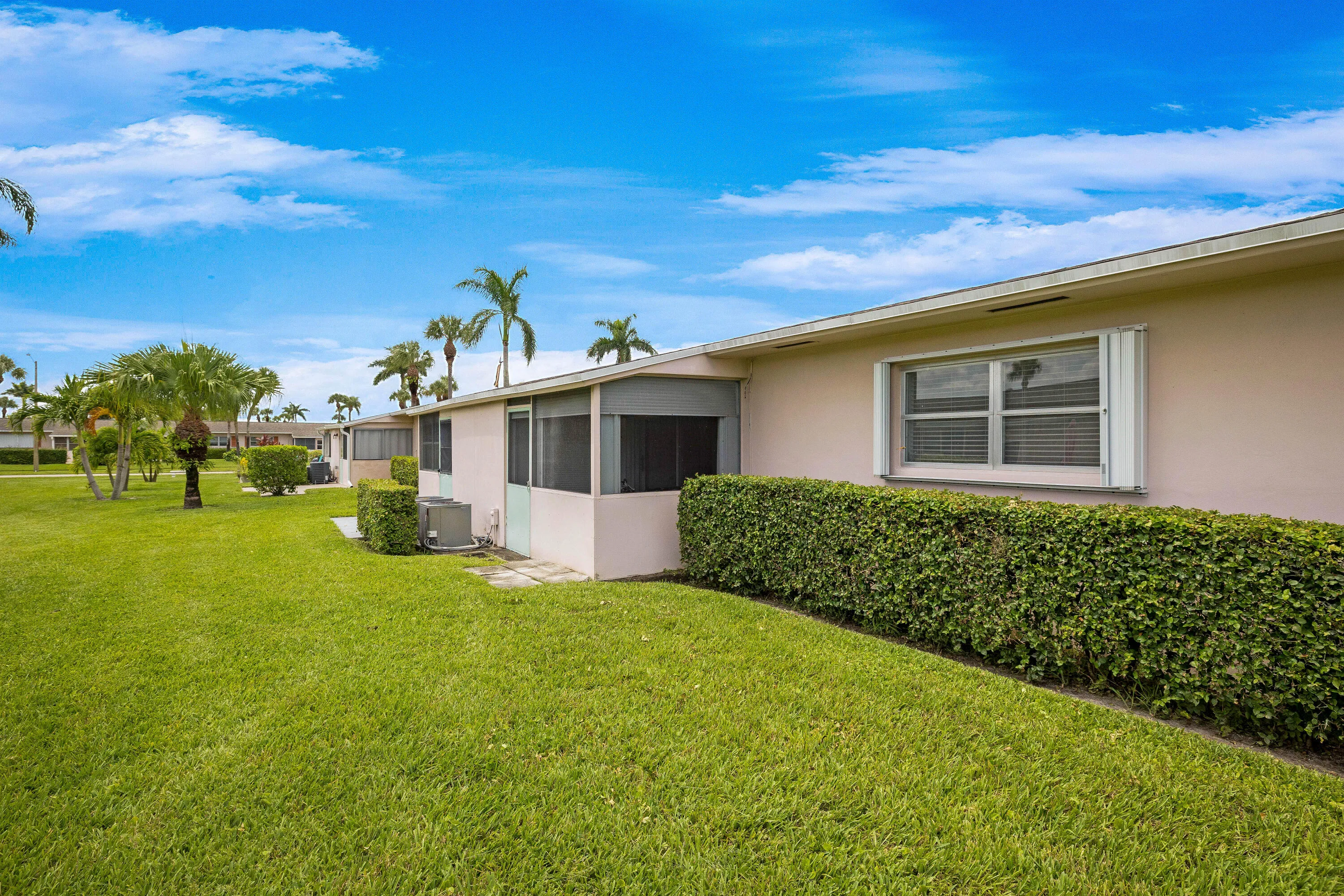 Screened patio, stucco exterior, window with hurricane shutters, manicured lawn, and mature palm trees