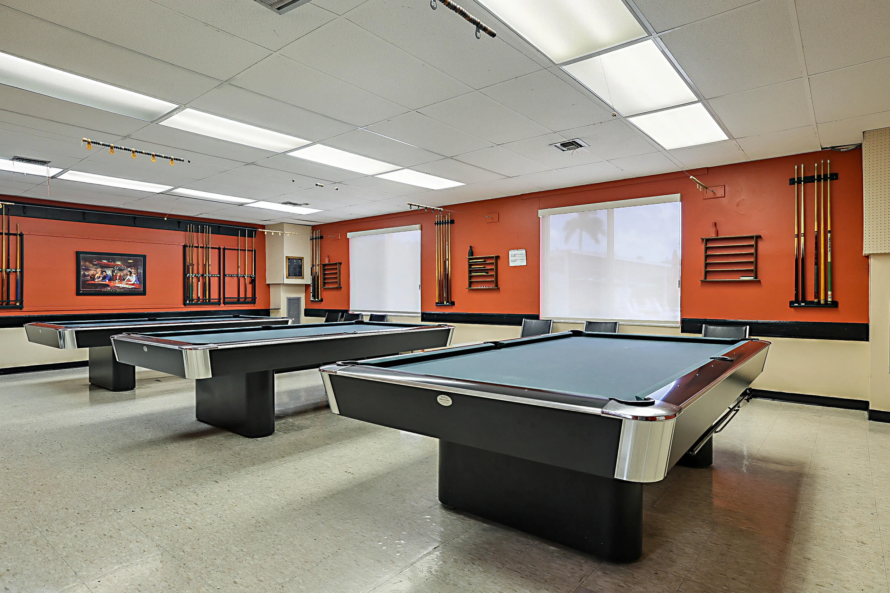 Recreation room featuring three billiard tables, overhead fluorescent lighting, and two large windows with roller shades