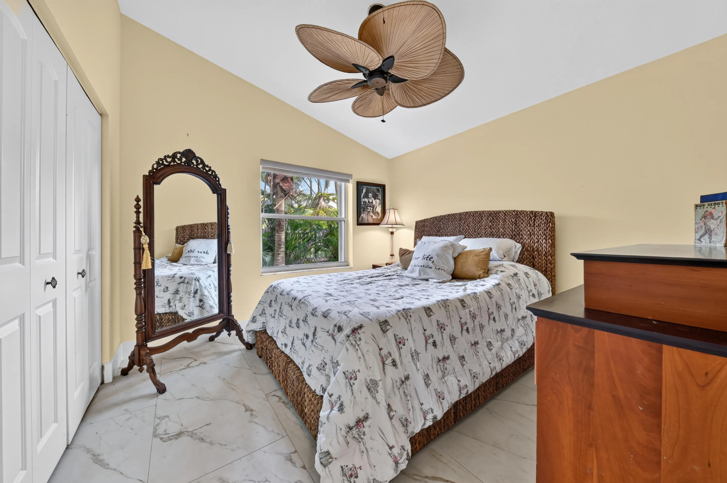 Vaulted ceiling with a tropical-style ceiling fan, large window with outdoor greenery, white bi-fold closet doors, and new tile flooring
