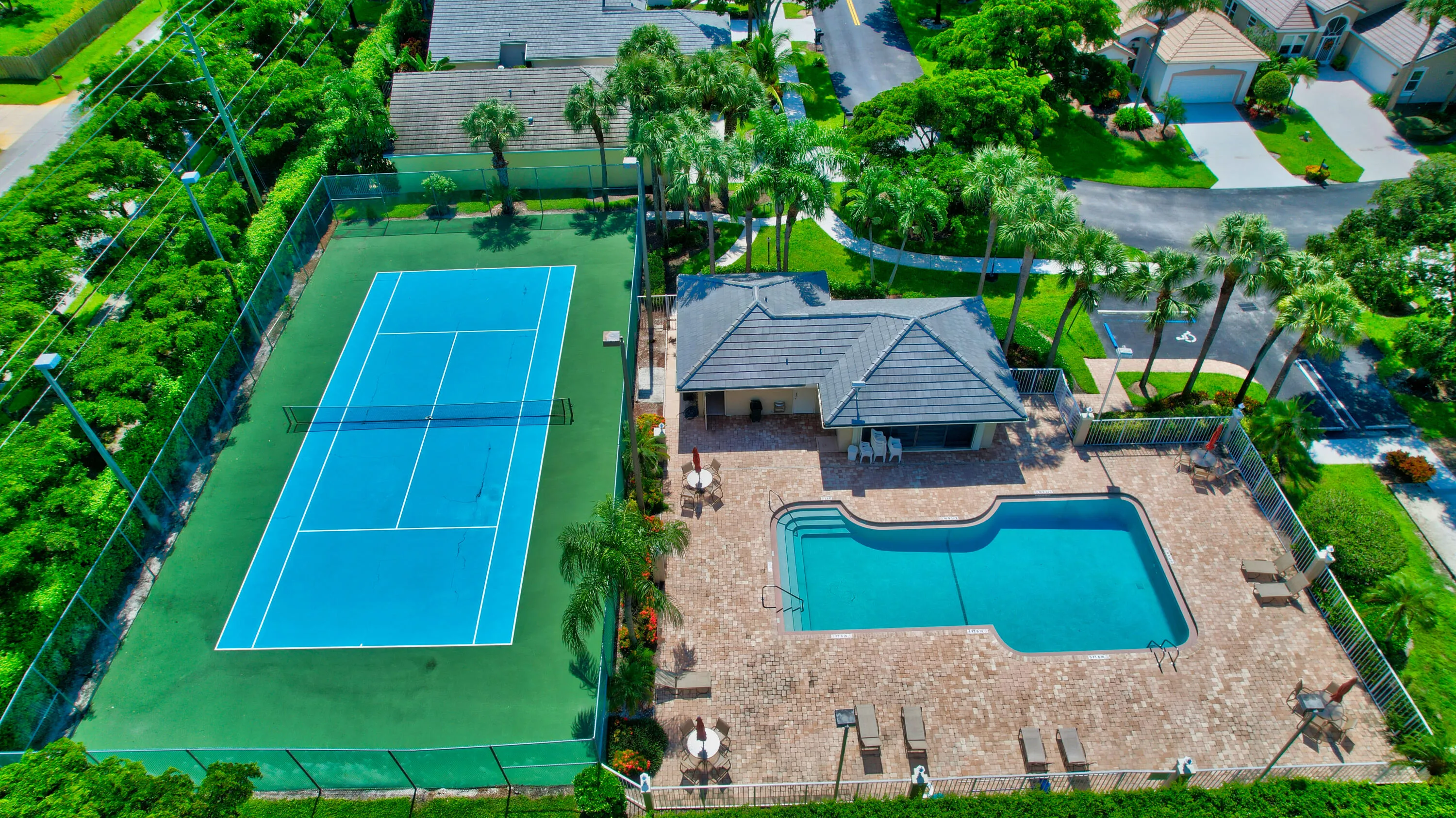 Swimming pool with paver decking, adjacent tennis court, and lush surrounding landscaping