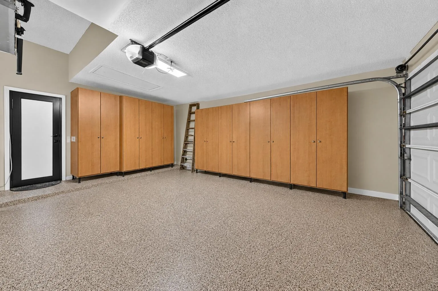 Garage featuring extensive built-in cabinetry, durable speckled floor coating, hurricane rated door and an automatic garage door opener