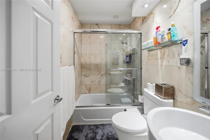 A beautifully appointed bathroom serving Secondary Bedrooms 2 and 3, featuring marble-inspired finishes, a glass-enclosed tub and shower, and a clean contemporary design.