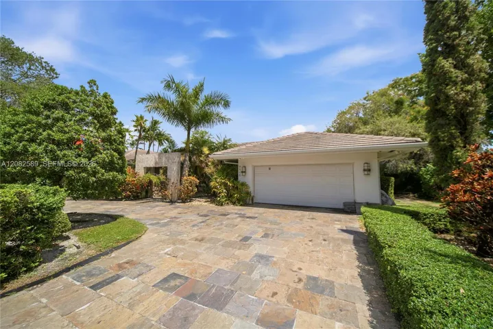 Spacious stone-paved driveway with an attached two-car garage, surrounded by lush tropical landscaping.