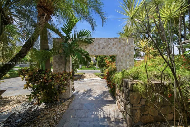 Tropical garden walkway framed by lush greenery and natural stone accents, creating a serene and inviting approach to the home.