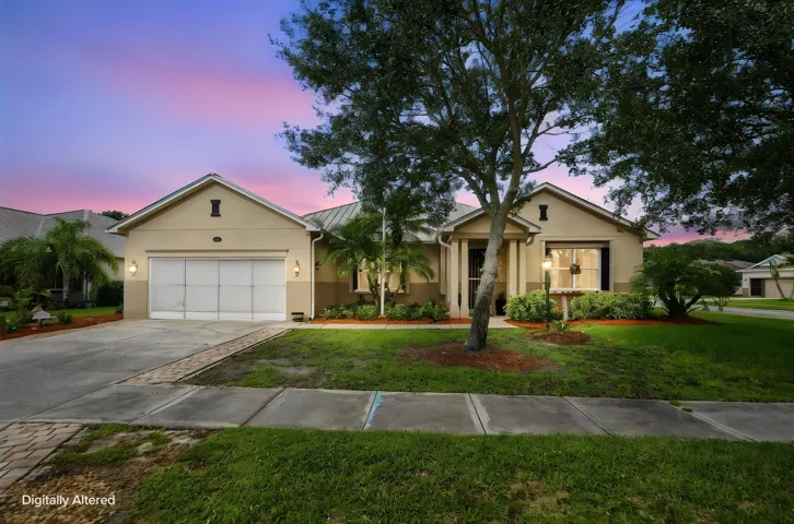 Stucco exterior with a metal roof, two-car garage, covered entry, and established landscaping