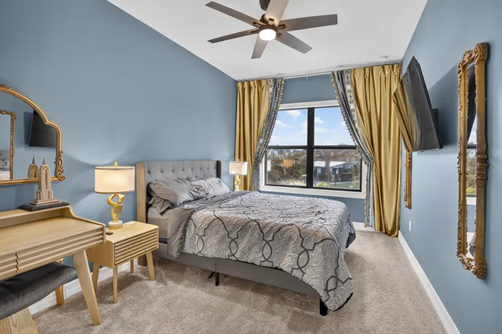 Carpeted bedroom featuring a ceiling fan, wall-mounted television, and a large window