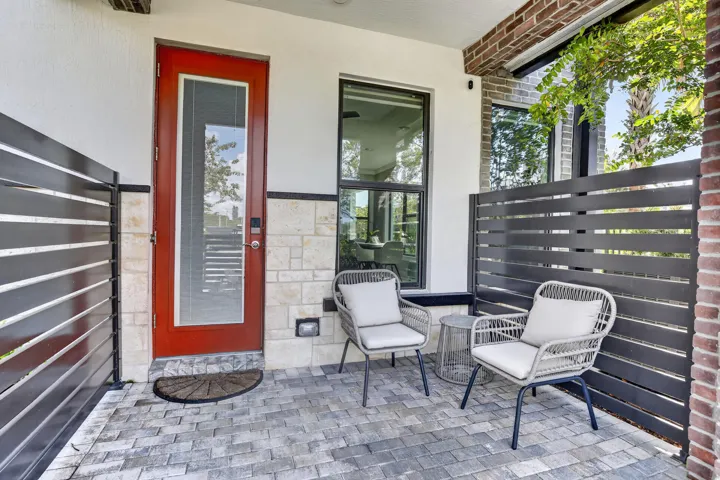 Welcoming front porch featuring a bold red entry door with sidelite window, horizontal slatted privacy screens, paver stone flooring, and comfortable seating areas ideal for outdoor relaxation