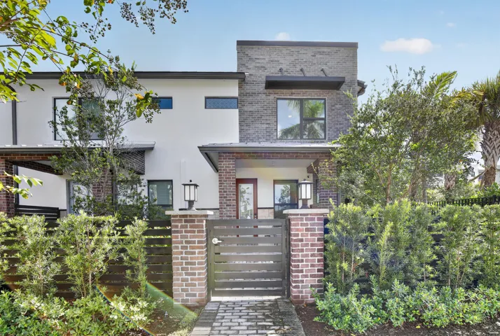 Modern architecture featuring brick and stucco exterior, a gated entry with paver walkway, and mature landscaping