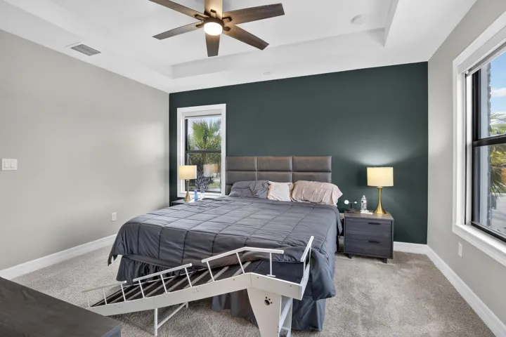 Tray ceiling with a ceiling fan, accent wall, and double windows with white trim