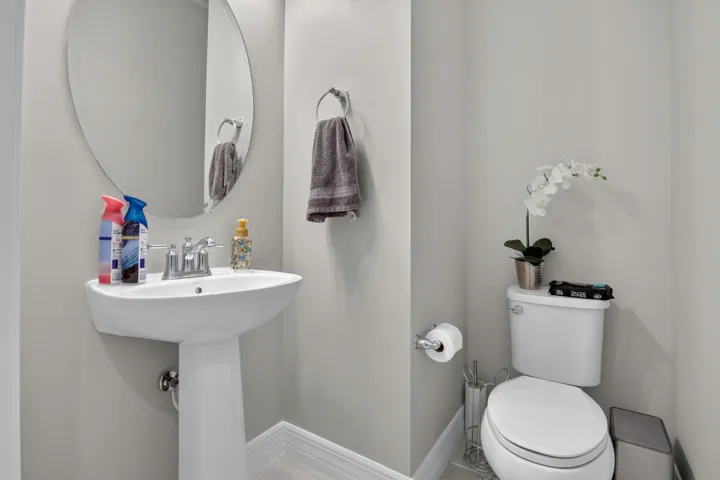 Pedestal sink with polished chrome faucet, oval frameless mirror, and a white toilet