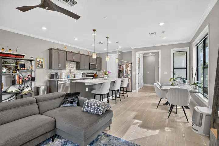 Open-concept living space featuring a gray upholstered sectional, wood-finish flooring throughout, and abundant natural light from large multi-pane windows