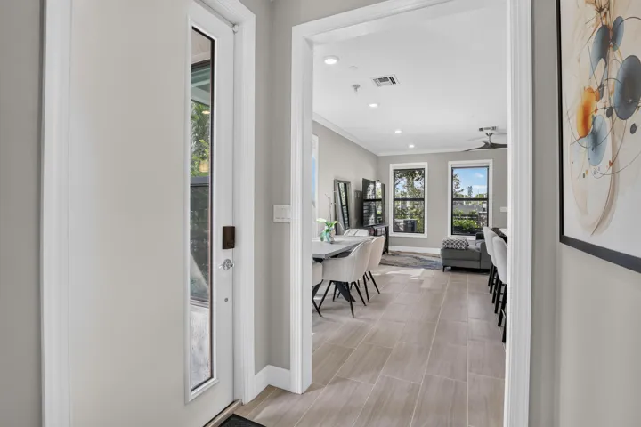 Entryway with a full-light door, leading to an open-concept living area featuring wood-finish tile flooring, recessed lighting, and multiple windows