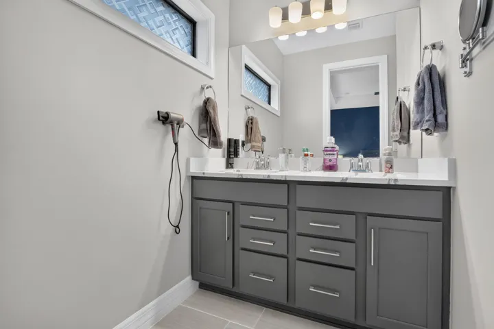 Dual vanity with gray cabinetry and brushed nickel hardware, white countertop, and individual sink basins