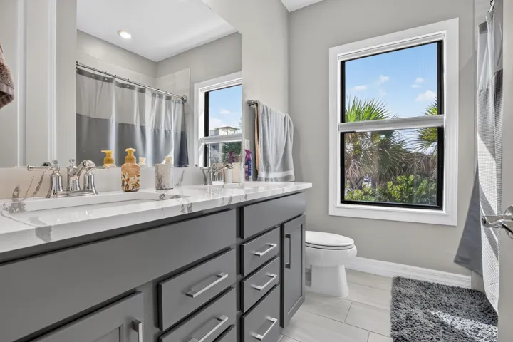 Dual vanity with a white countertop and undermount sinks, gray cabinetry with modern hardware, framed mirror, and a walk-in shower with a shower curtain