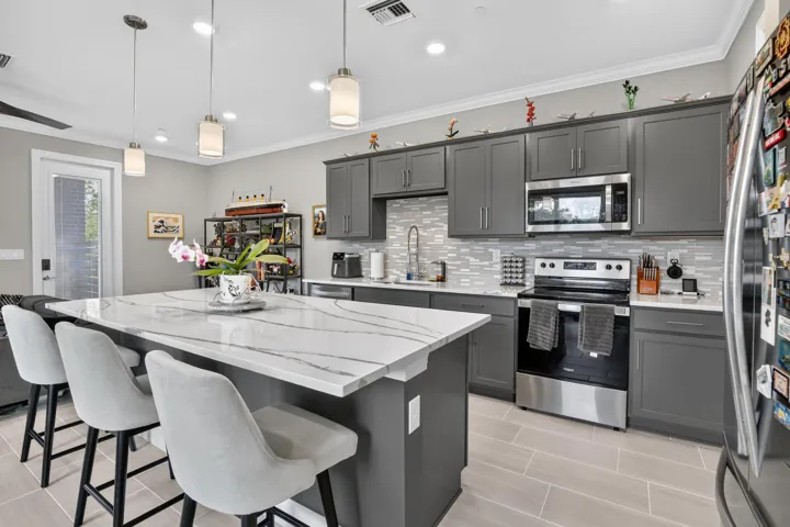 Kitchen featuring an expansive island with a stone-finish countertop, gray cabinetry, stainless steel appliances, and a tiled backsplash