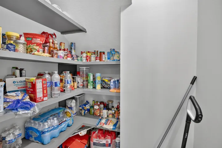 Walk-in pantry featuring built-in shelving, white walls, and a corner configuration