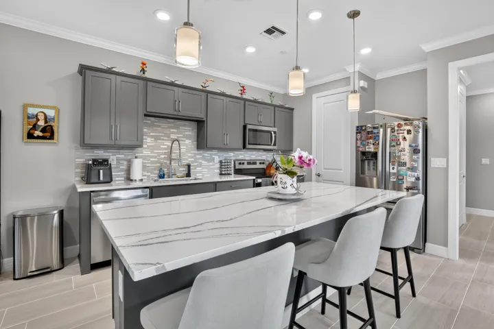 Modern kitchen featuring gray cabinetry, a mosaic tile backsplash, stainless steel appliances, and a substantial island with a white countertop