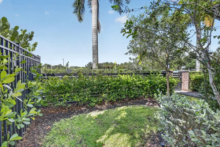 Mature landscaped grounds featuring a manicured lawn, lush perimeter hedging, decorative mulch beds, and established trees including a tall palm specimen
