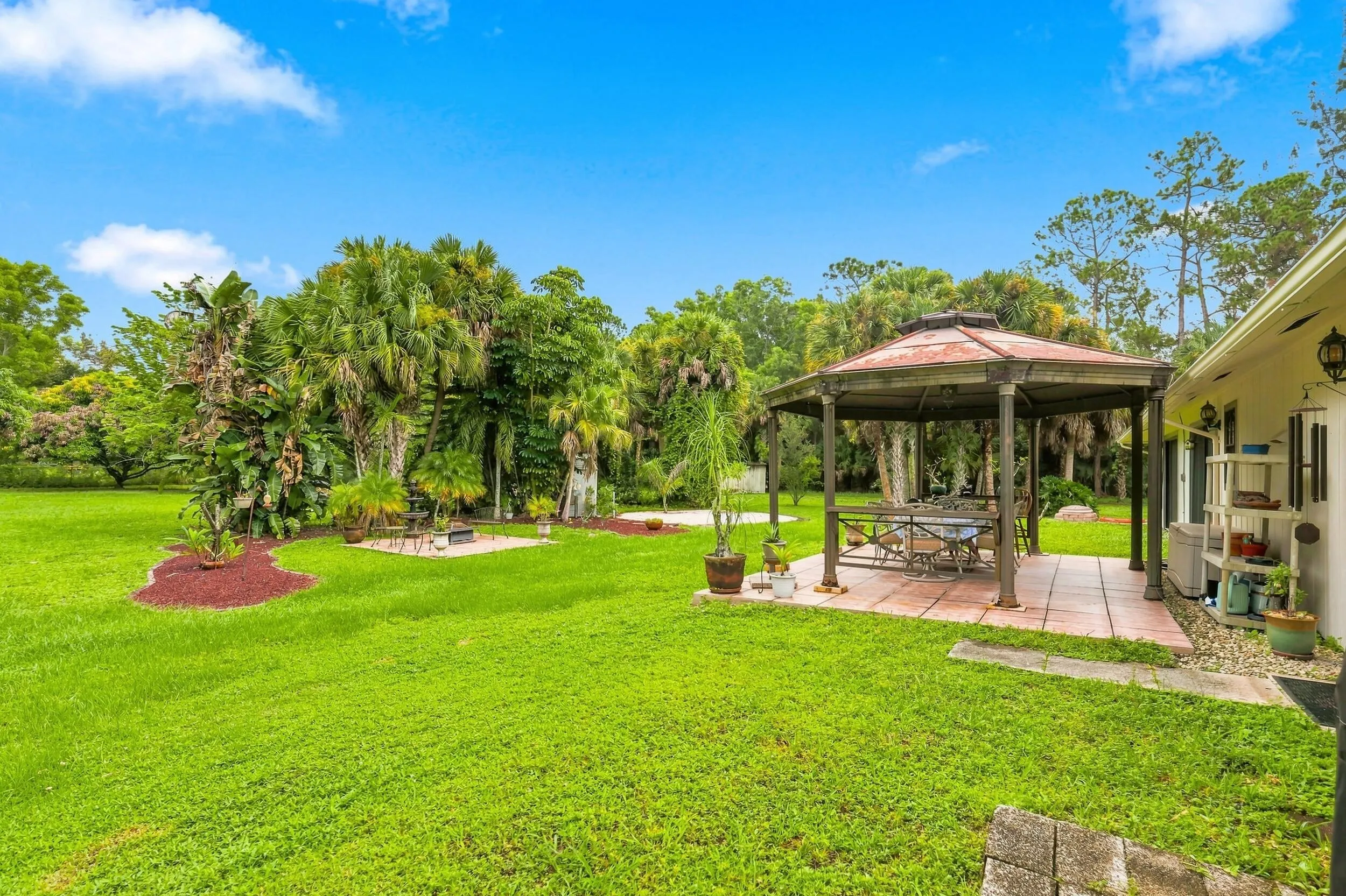 Large grassy backyard with mature tropical landscaping and a covered gazebo for outdoor enjoyment.