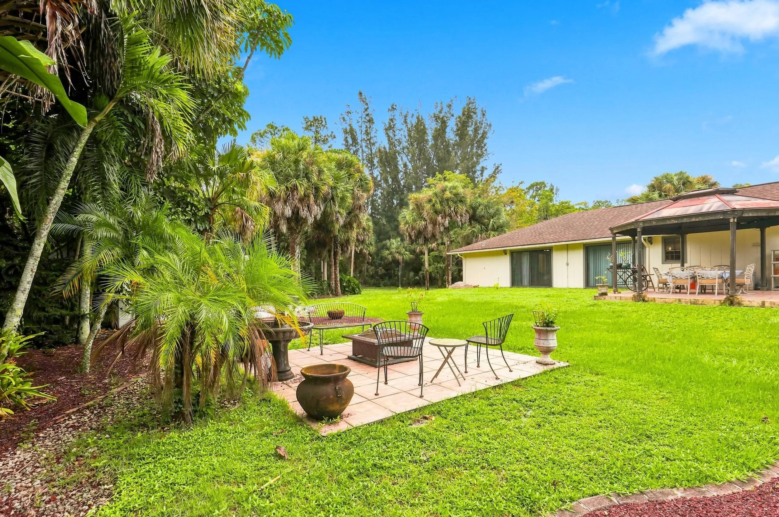 Expansive backyard with open lawn, mature tropical landscaping, and a patio area for outdoor enjoyment.