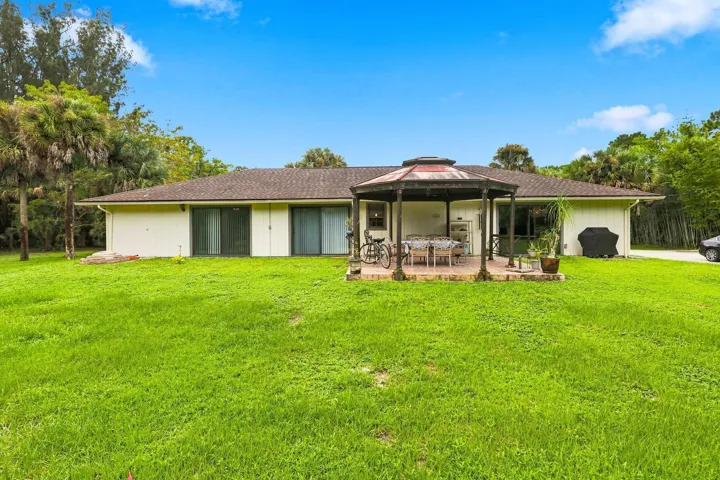Wide rear view showcasing the home, large grassy backyard, mature trees, and covered outdoor area.