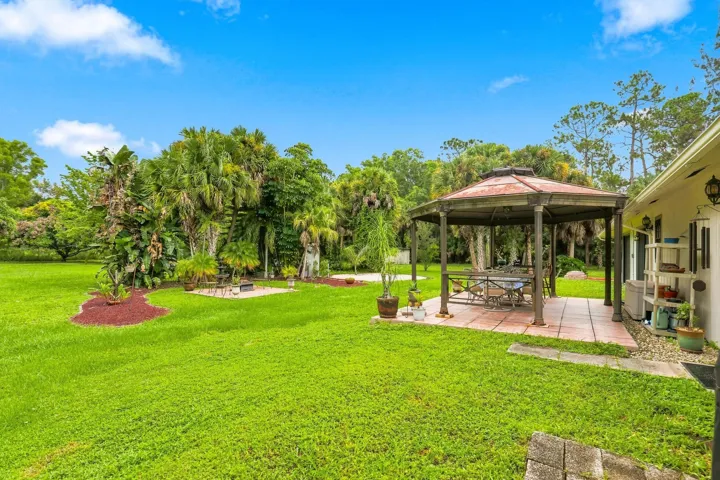 Large grassy backyard with mature tropical landscaping and a covered gazebo for outdoor enjoyment.
