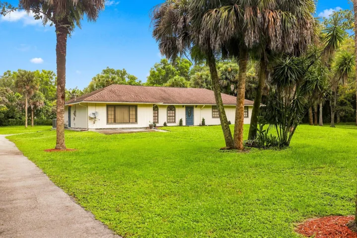 Front view of the single-story home set back on a spacious lot with mature palm trees and open lawn.