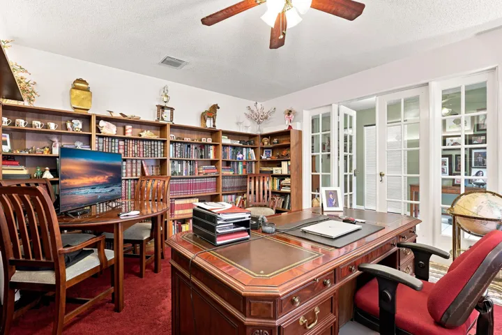 Spacious dedicated office featuring extensive built-in shelving, ceiling fan, and plenty of workspace.