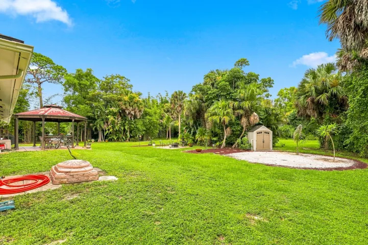 Spacious backyard featuring open lawn, mature trees, and a covered outdoor gathering area.