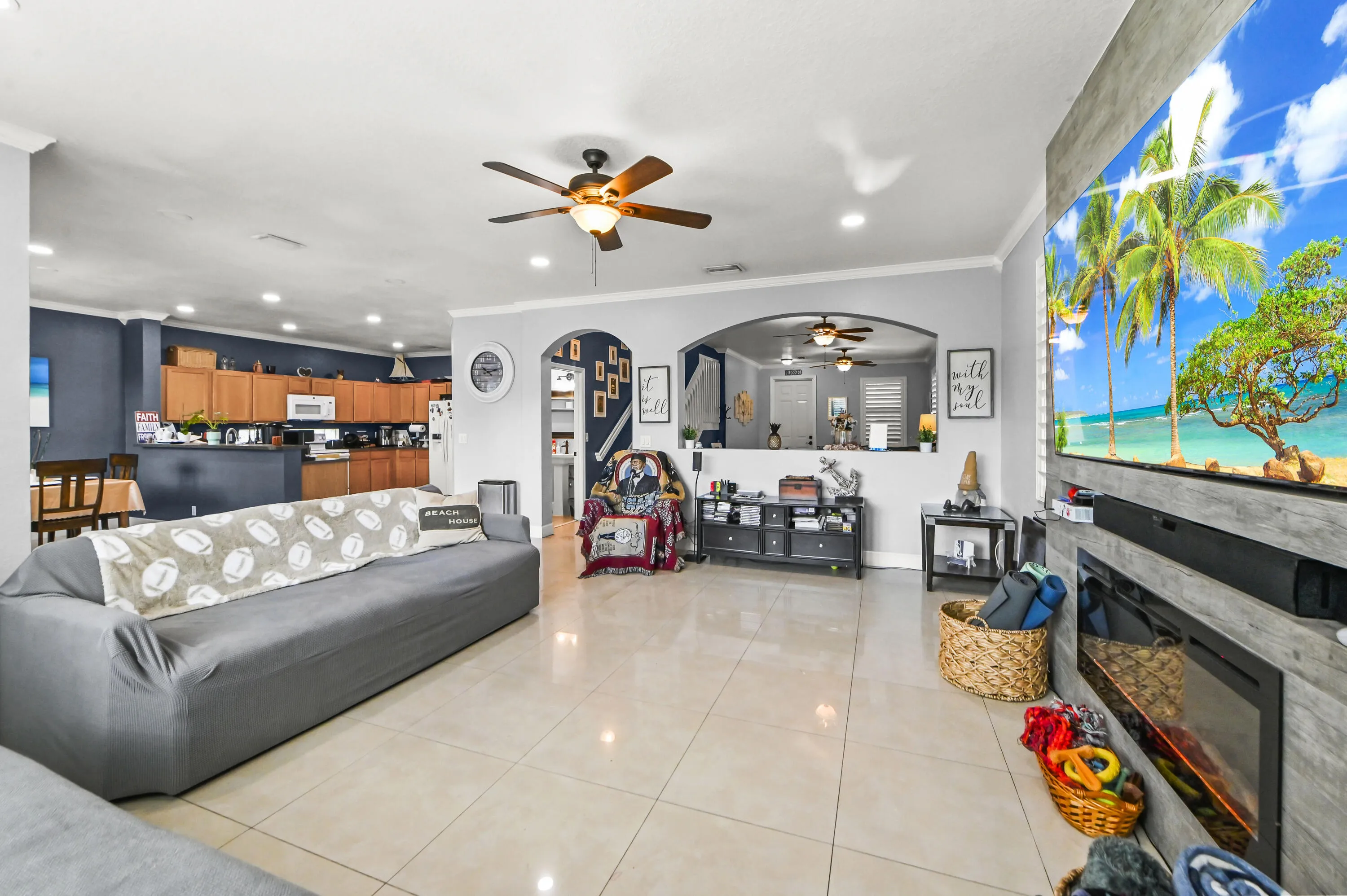 Open-concept living area featuring polished tile flooring, a ceiling fan with integrated lighting, and a wood-finish kitchen cabinetry with stainless steel appliances