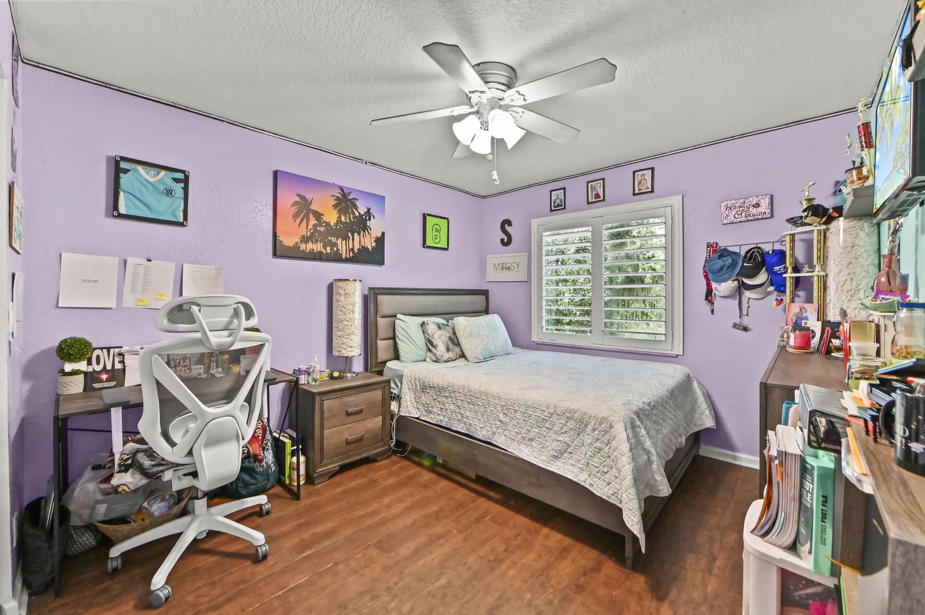 Bright bedroom featuring lavender walls, wood-finish flooring, and a ceiling fan with integrated lighting