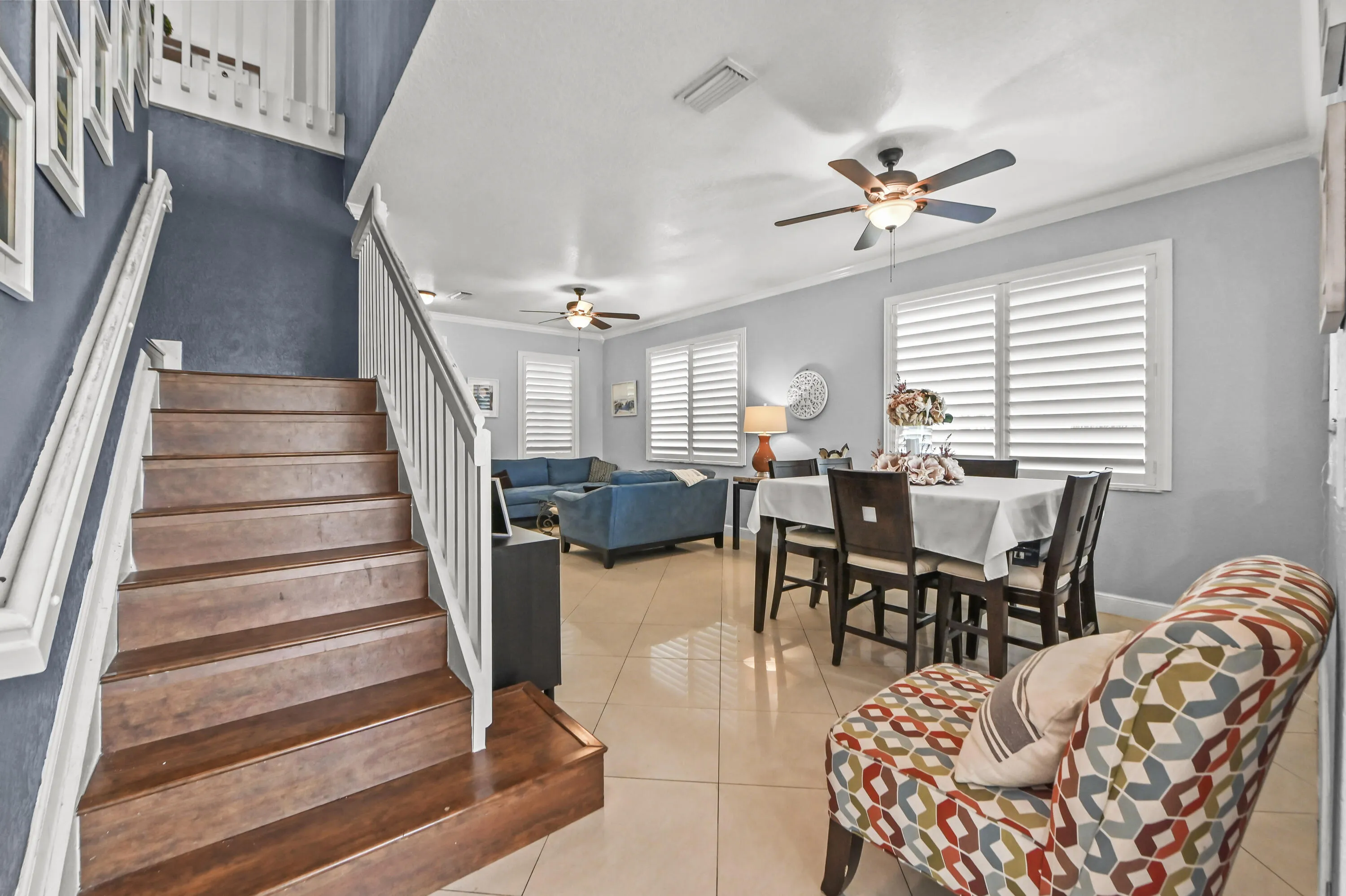 Wood-finish staircase with white railings, tile flooring, and multiple ceiling fans
