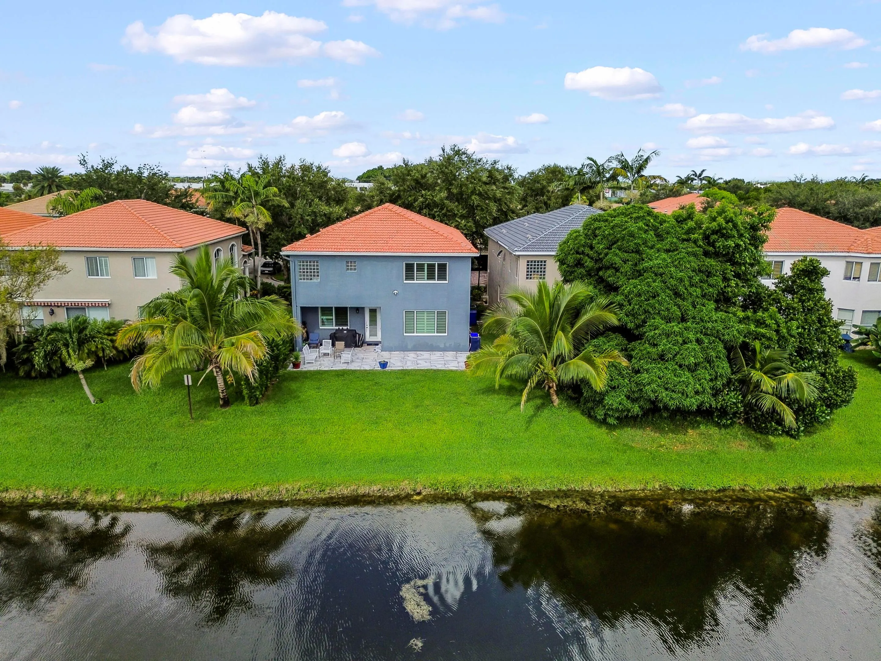 Waterfront property featuring a well-maintained lawn, mature palm trees, and an exterior patio area