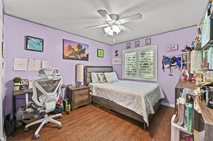 Bright bedroom featuring lavender walls, wood-finish flooring, and a ceiling fan with integrated lighting