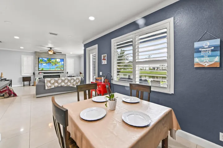 Open-concept living space featuring a dining area with wood-finish table and chairs, polished tile flooring throughout, and expansive windows with plantation shutters