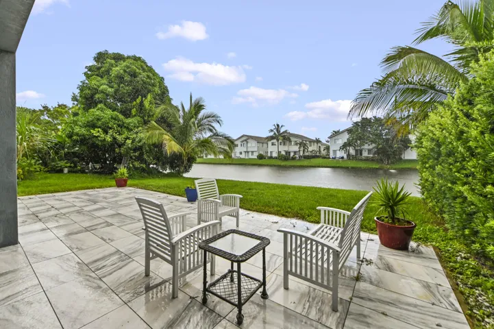 Expansive patio with large format paver tiles, mature tropical landscaping, and water frontage