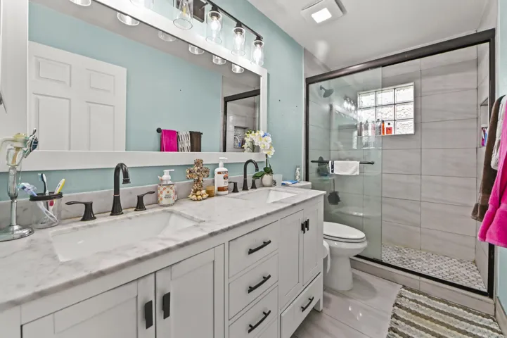 Spa-inspired primary bathroom featuring dual vanities with white cabinetry, marble-finish countertops, and matte black fixtures