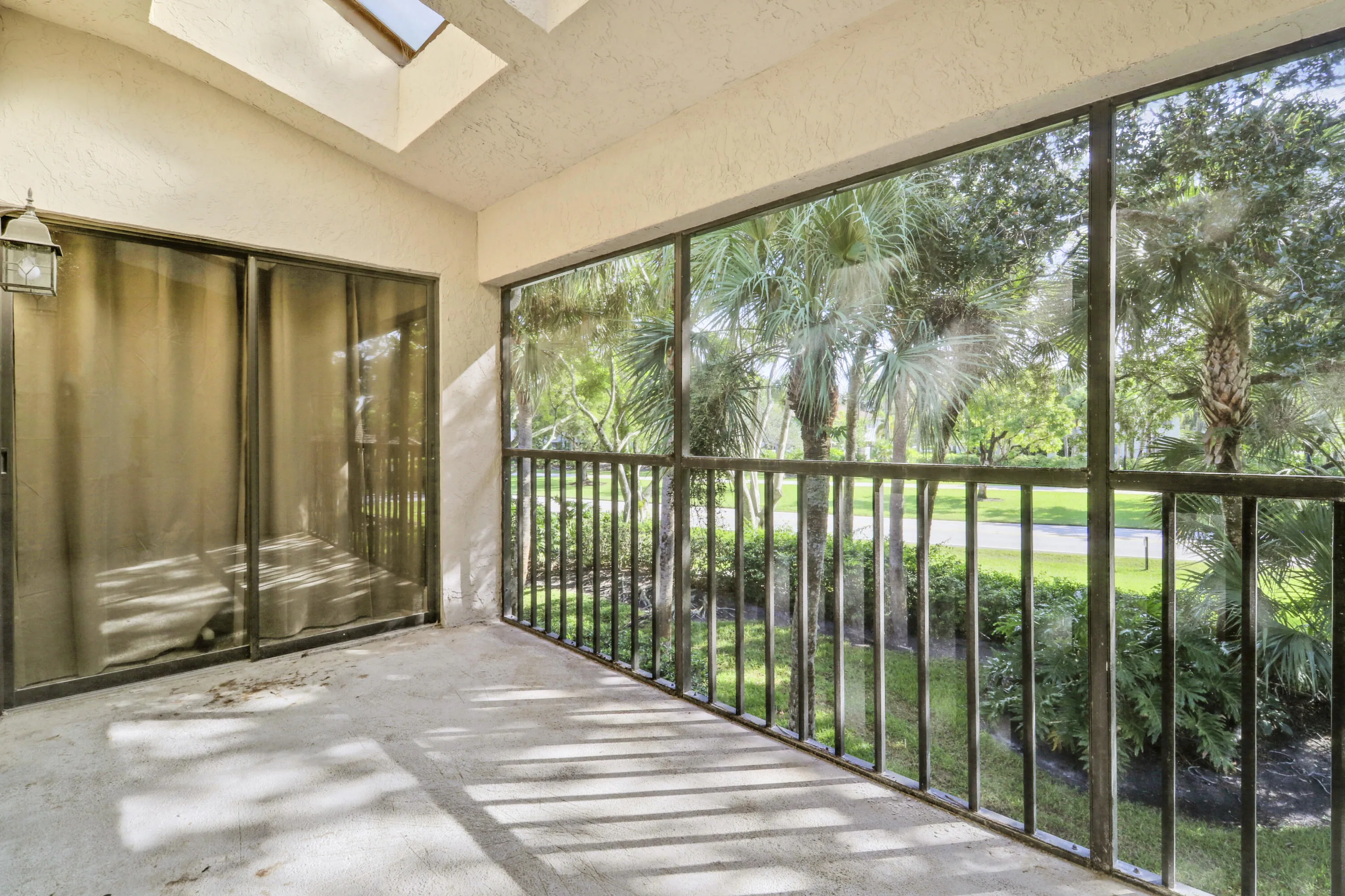 Screened balcony featuring a skylight, exterior wall lantern, sliding glass doors, and tropical landscaping