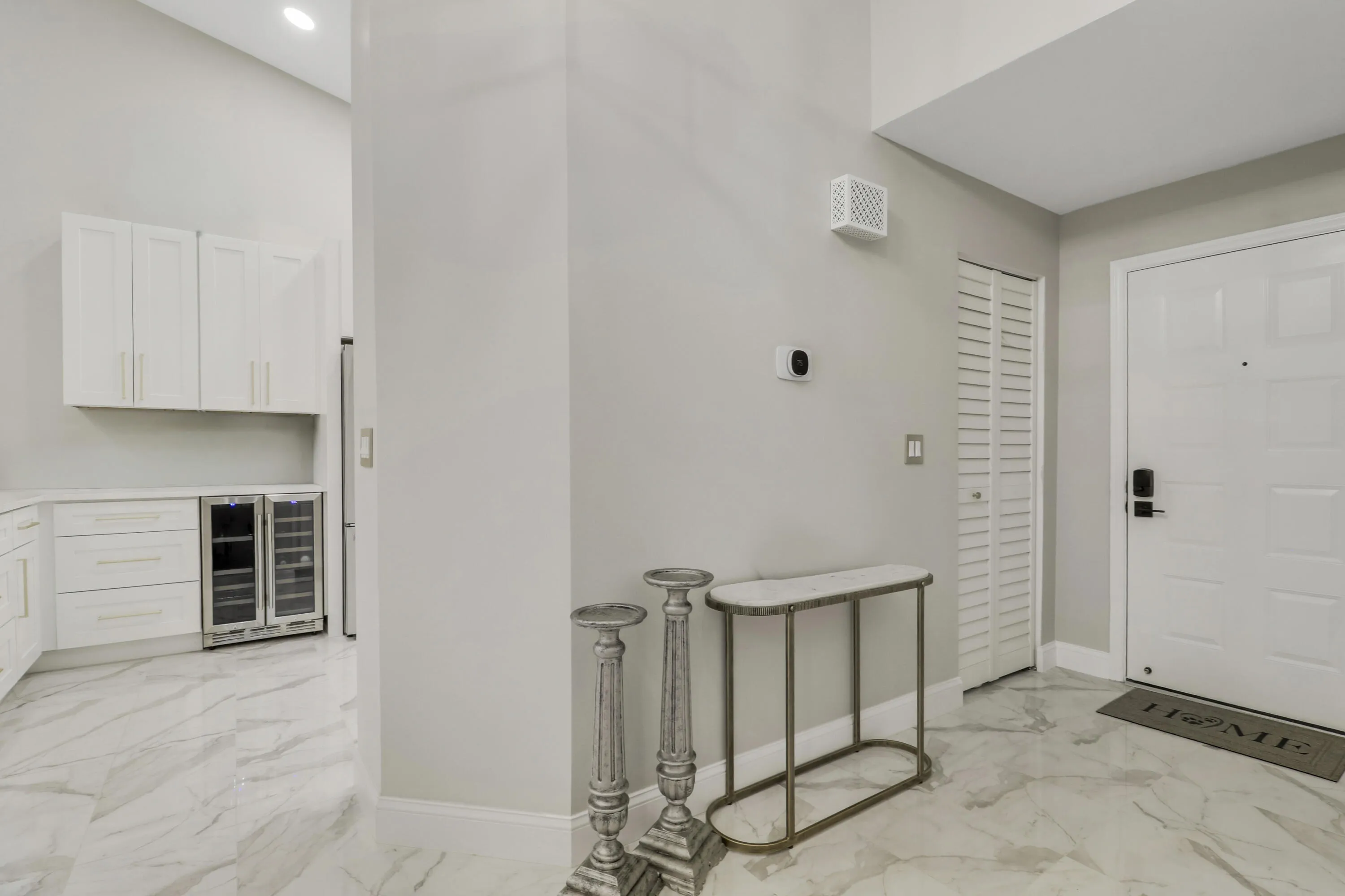 White paneled entry door with dark hardware, louvered utility door, and marble-look tile flooring