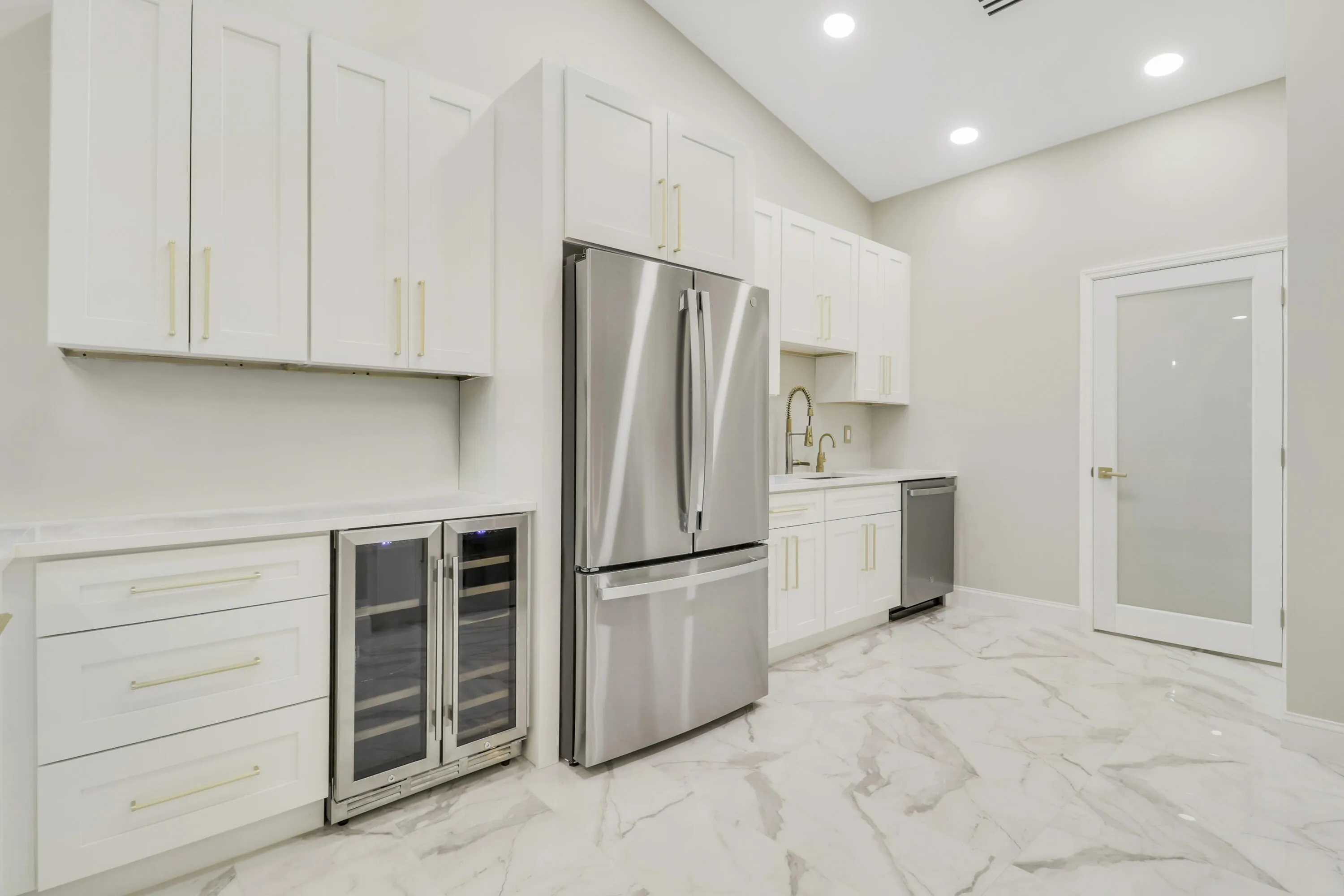 Vaulted ceilings, white shaker-style cabinetry, stainless steel appliances, a built-in beverage cooler, and marble-look tile flooring