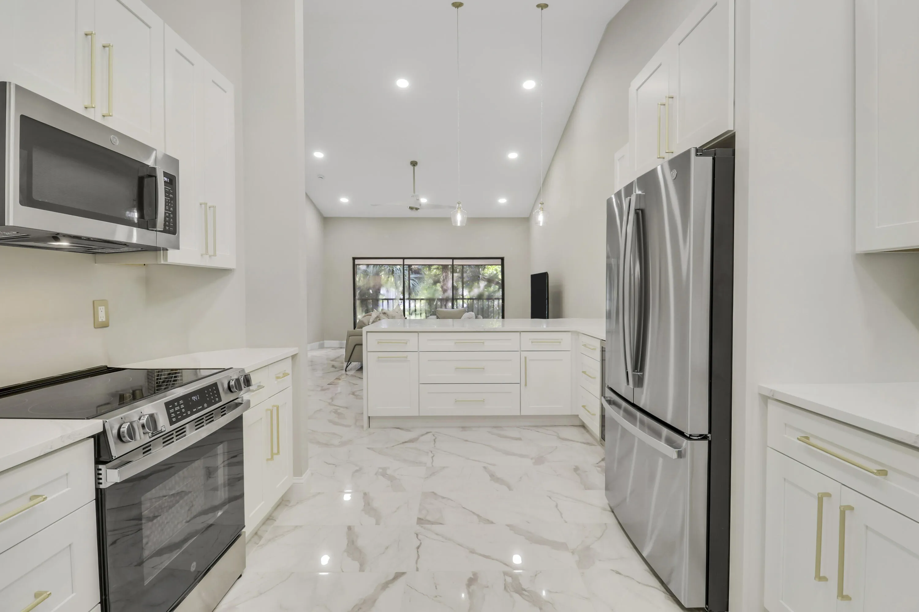 Contemporary kitchen featuring stainless steel appliances, white cabinetry with gold-tone hardware, and light-toned, veined tile flooring