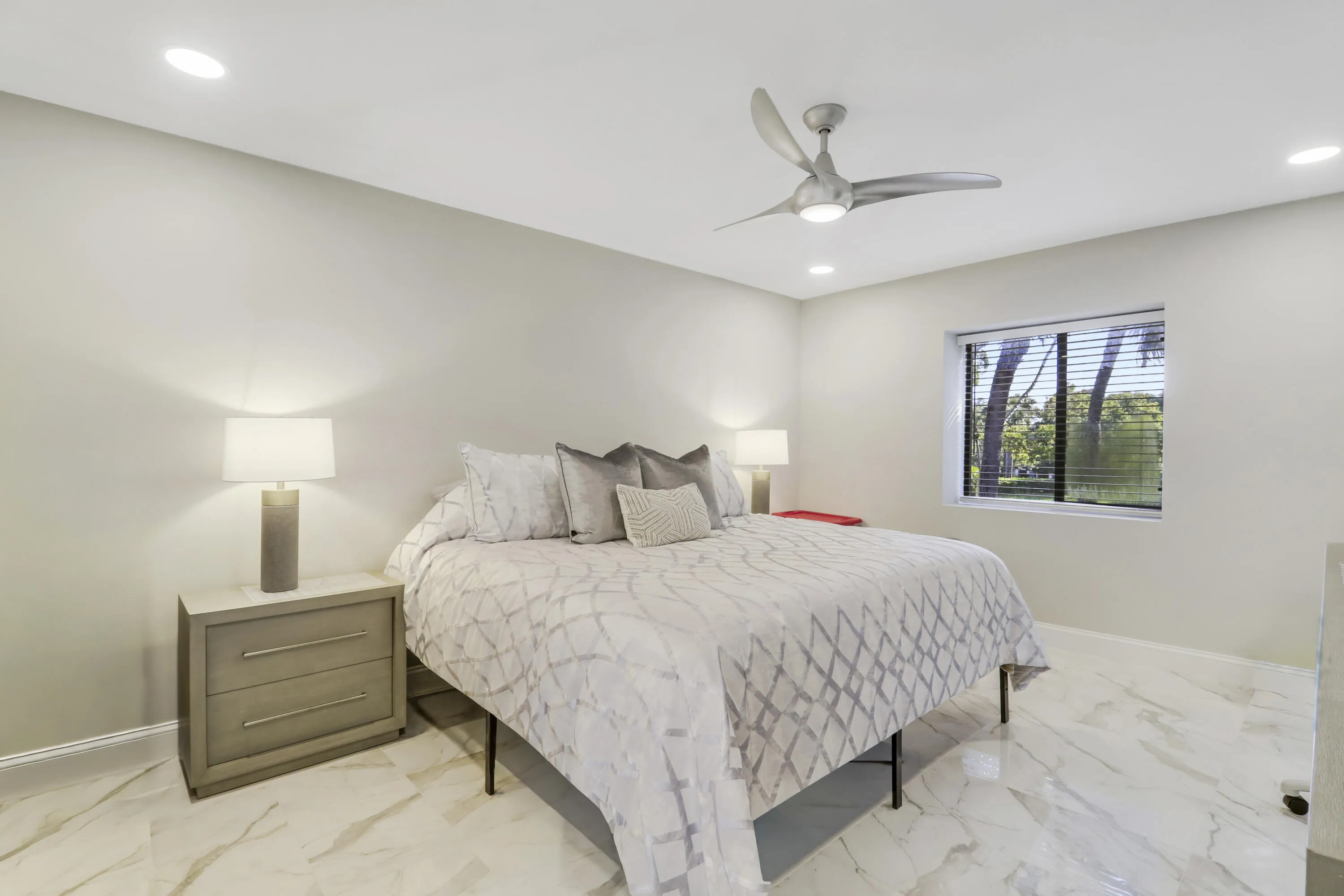 Recessed ceiling lighting, modern ceiling fan, large window with blinds, light-toned walls, and marble-look tile flooring
