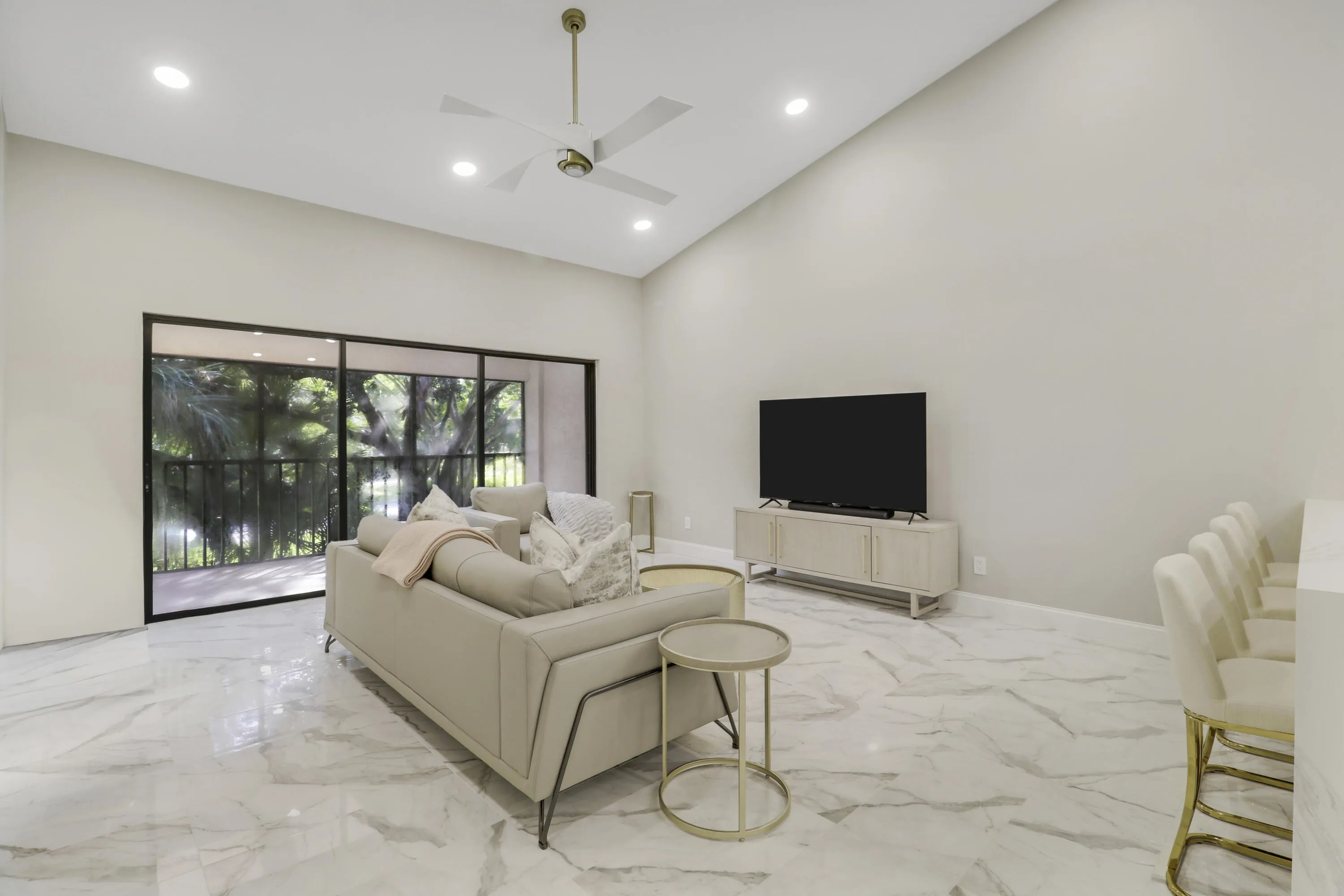 Vaulted ceiling with recessed lighting and ceiling fan, large format marble-look tile flooring, and expansive sliding glass doors opening to a balcony