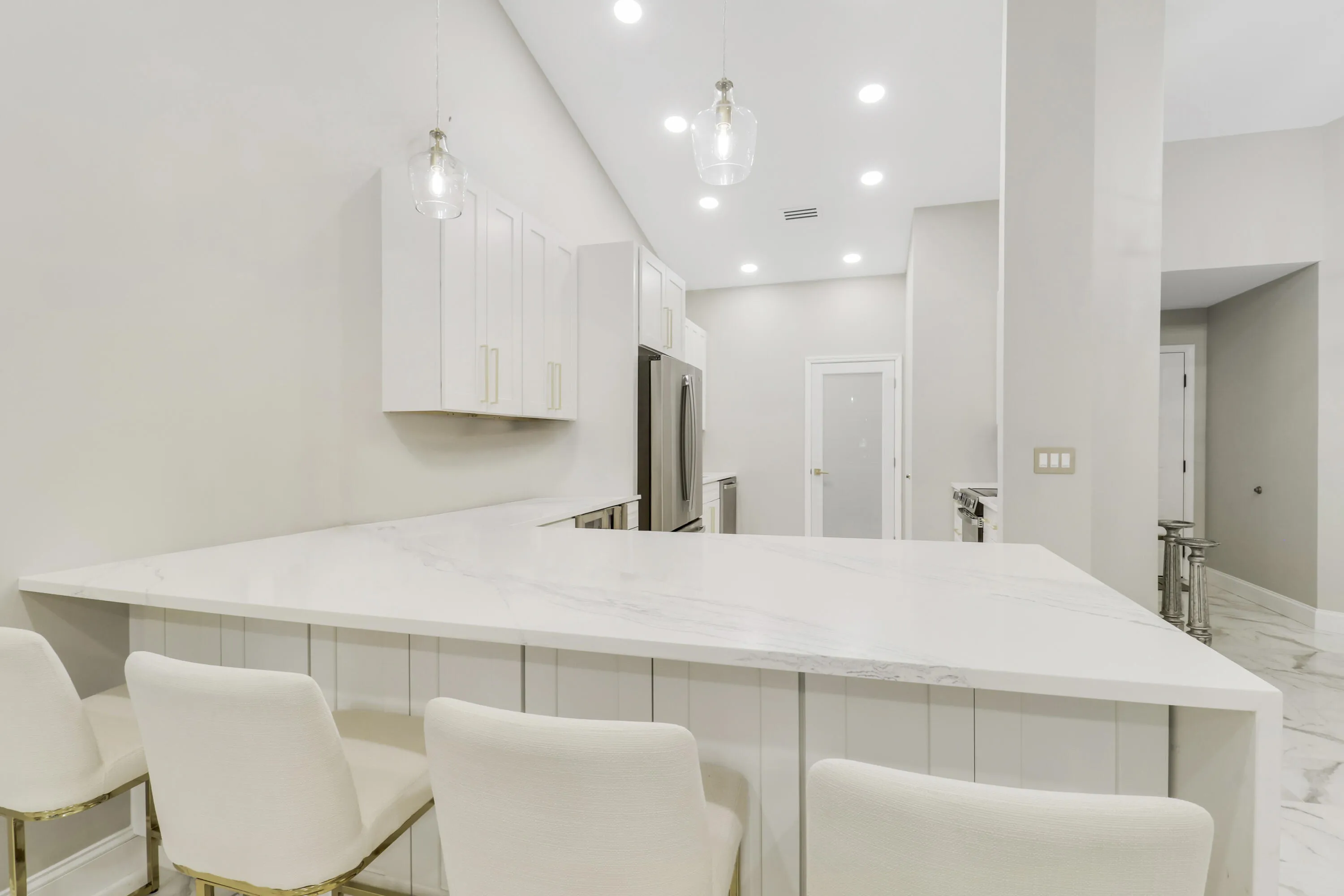 U-shaped kitchen island with white countertop, white cabinetry with gold-tone hardware, stainless steel appliances, and recessed lighting