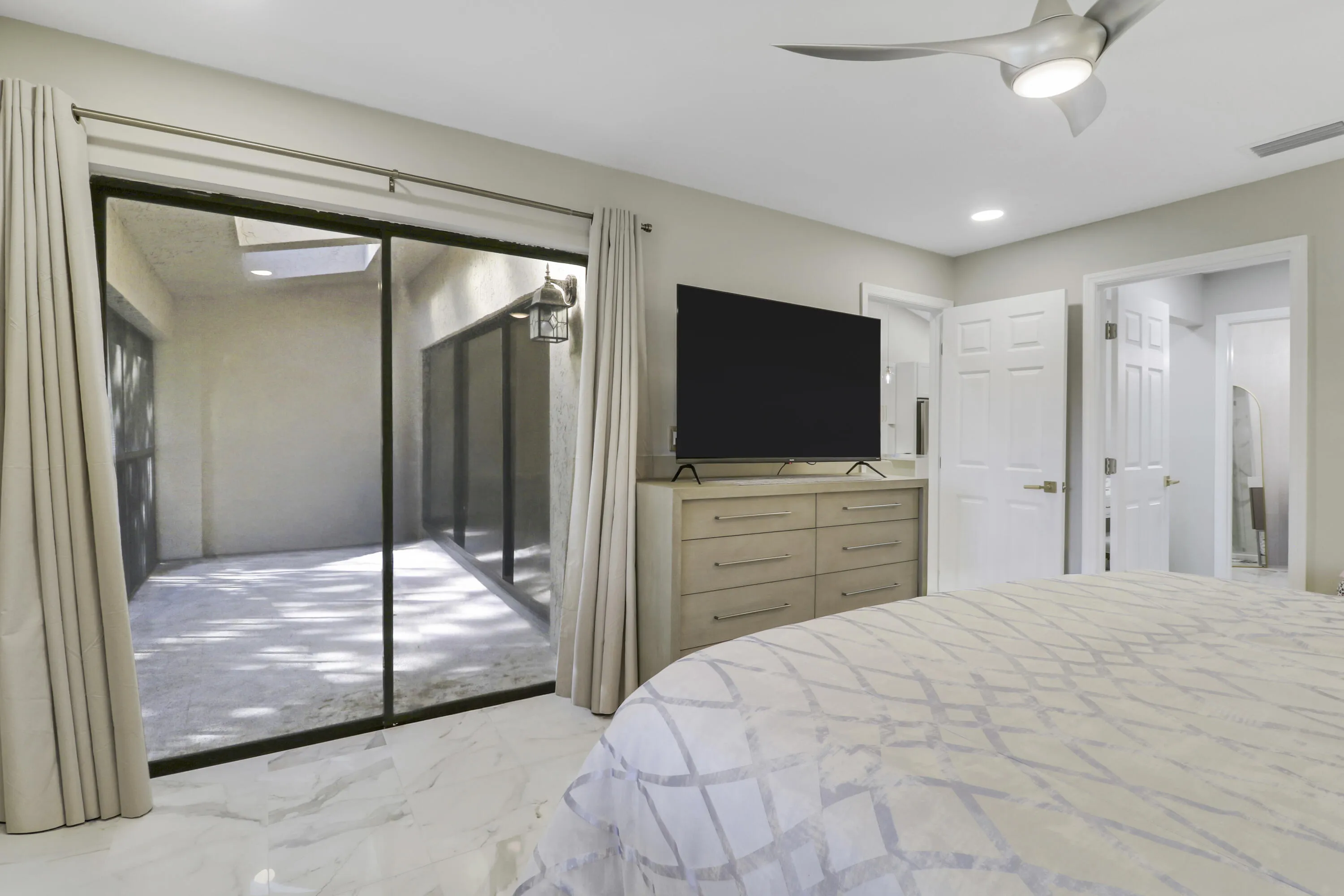 Sliding glass doors opening to a private patio, modern ceiling fan with integrated lighting, and white tile flooring