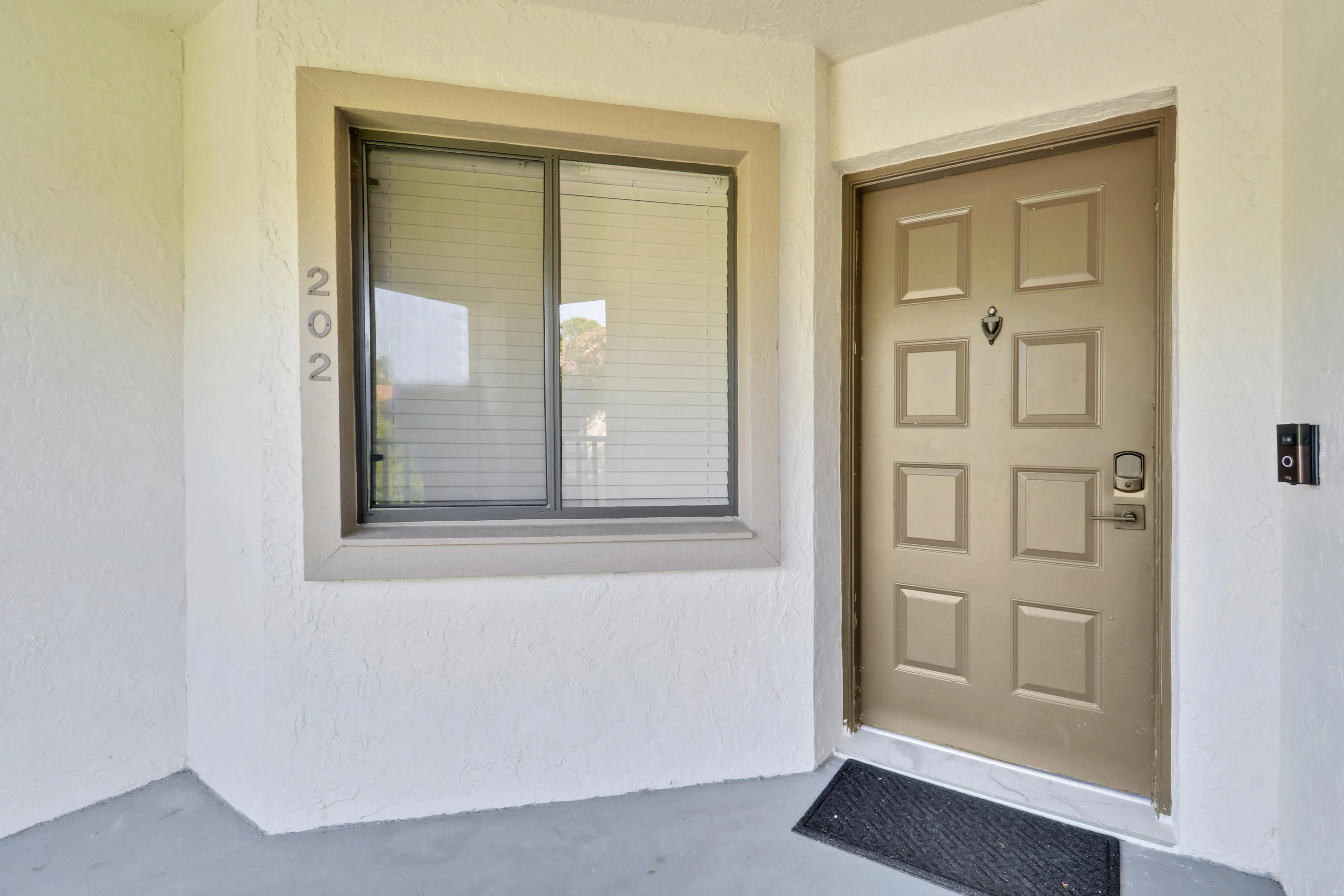 Textured exterior wall finish, framed window with blinds, panel-style entry door, and wall-mounted intercom system