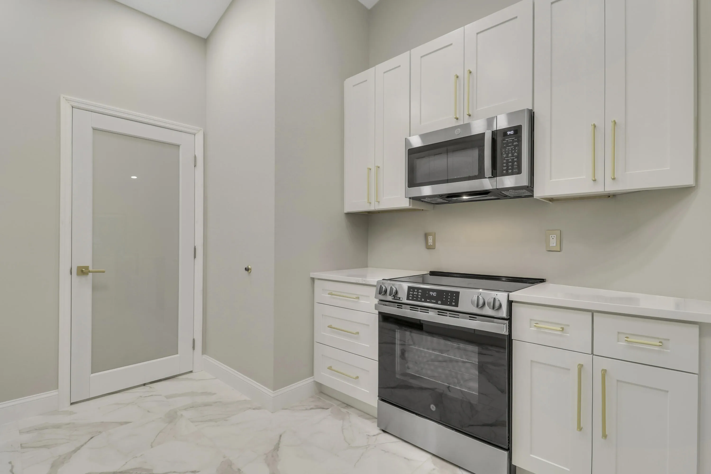 Kitchenette with white shaker cabinetry, stainless steel appliances, light-colored countertops, and marble-look flooring
